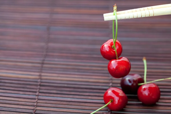 Cherry and chopsticks on bamboo mat — Stockfoto