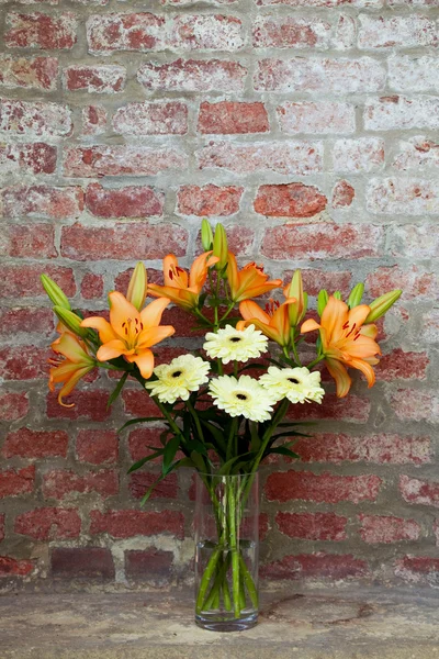 Flowers in a vase standing in the background of a brick wall