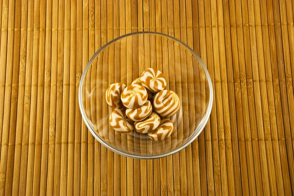 Caramelo en un tazón de vidrio en una estera de bambú —  Fotos de Stock