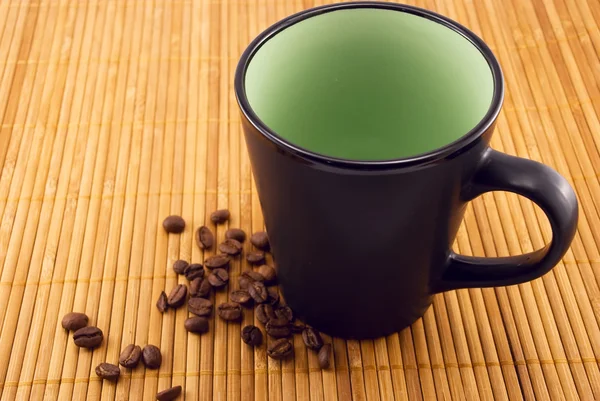 Taza y granos de café en una estera de bambú —  Fotos de Stock