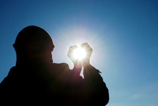 Человек держит солнце в руках против неба — стоковое фото