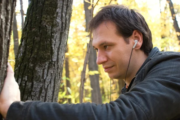Man met hoofdtelefoon permanent in de buurt van de boom — Stockfoto
