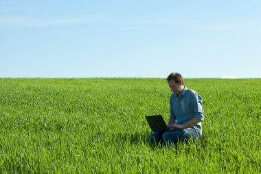 Young man using laptop in the field clipart