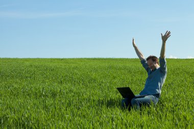 Young man using laptop in the field clipart