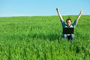 Young man using laptop in the field clipart