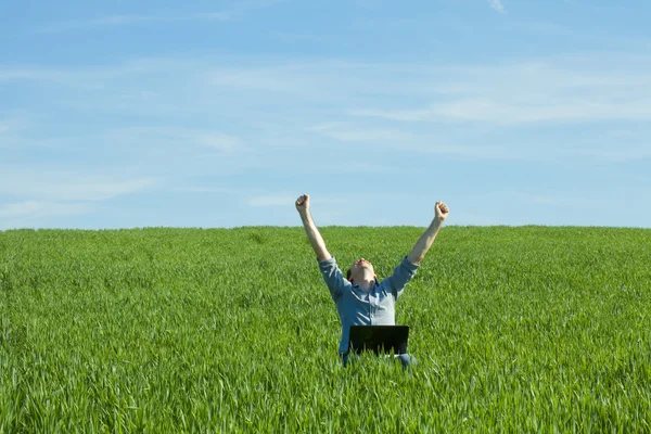 Молодой человек с ноутбуком в поле — стоковое фото