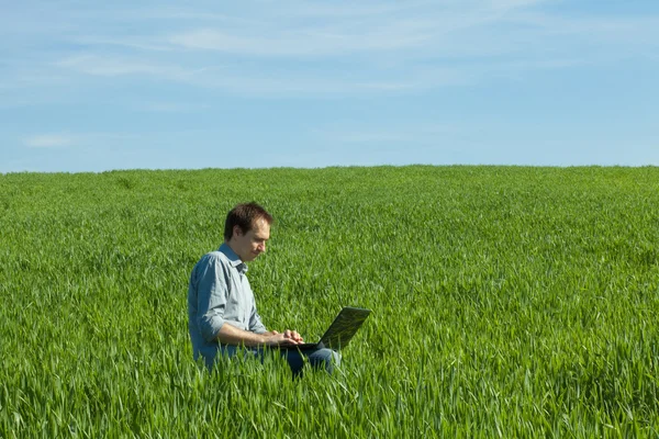 Jonge man met laptop in het veld — Stockfoto