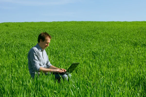 Joven usando el ordenador portátil en el campo — Foto de Stock