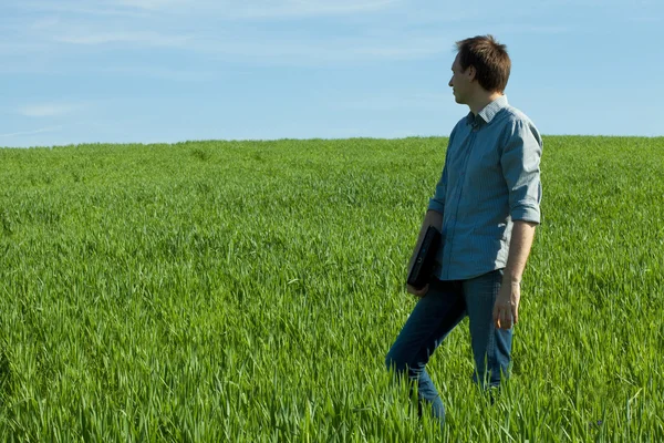 Jeune homme debout avec un ordinateur portable dans le champ vert — Photo