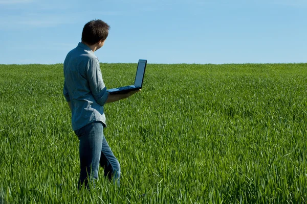 Jovem de pé com um laptop no campo verde — Fotografia de Stock