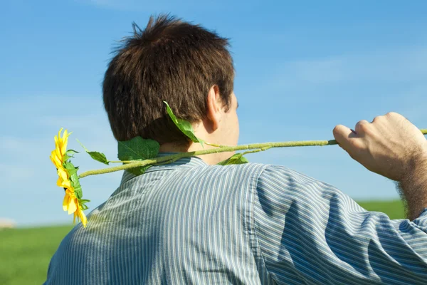 Young man standing with a sunflower in the green field — Stock Photo, Image