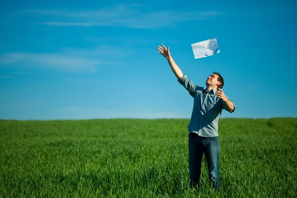若い男が、緑の野原で、紙を投げ — ストック写真