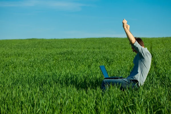 Молодой человек с ноутбуком в поле — стоковое фото