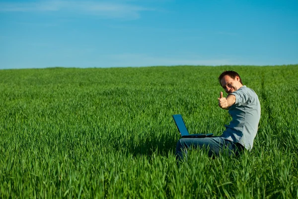 Νεαρός άνδρας, χρησιμοποιώντας φορητό υπολογιστή στο πεδίο — Φωτογραφία Αρχείου