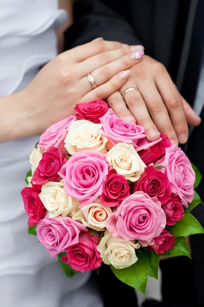 The hands of the bride and groom lying on the bridal bouquet — Stock Photo, Image