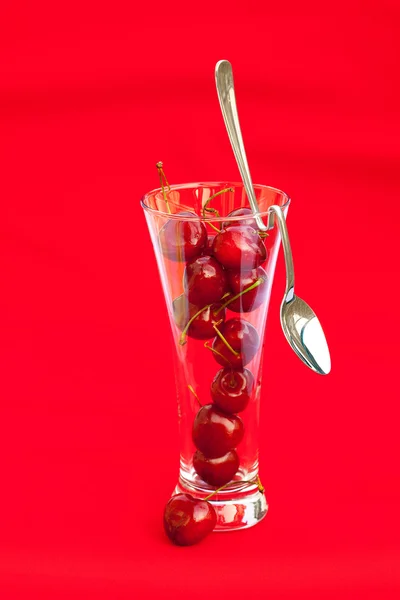 Sklenka cherry a lžící na červeném pozadí — Stock fotografie