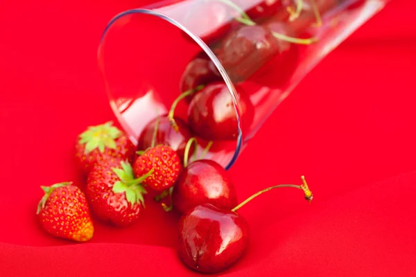 Szklanka wiśni i truskawka na czerwonym tle — Zdjęcie stockowe