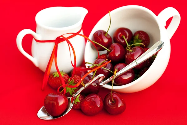牛奶壶丝带樱桃和草莓红色背景上 — 图库照片