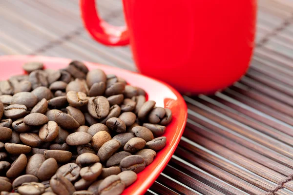 カップとソーサーと竹のマットの上のコーヒー豆 — ストック写真