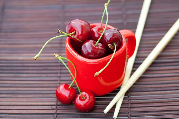 Cherry cup en stokjes op bamboe mat — Stockfoto