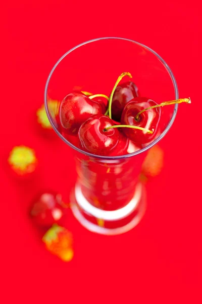 Glass av kirsebær og jordbær på rød bakgrunn – stockfoto