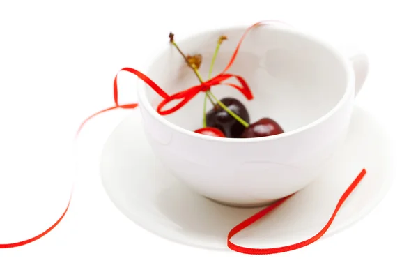 Кубок блюдце и вишни с лентой изолированы на белом — стоковое фото