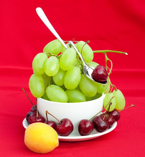 Löffel Trauben Kirsche und Aprikose in der Tasse auf rotem Hintergrund — Stockfoto