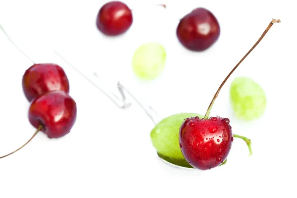Cerezas con gotas de agua en una cuchara y una uva aislada en — Foto de Stock