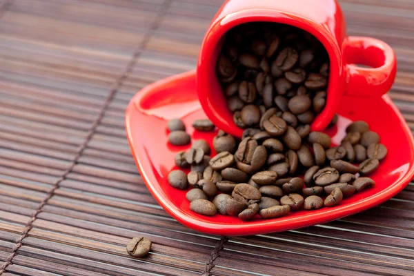 Xícara vermelha com grãos de café em uma esteira de bambu — Fotografia de Stock