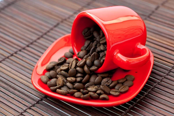 Bambu hasırının üzerinde kahve çekirdekleri olan kırmızı fincan. — Stok fotoğraf
