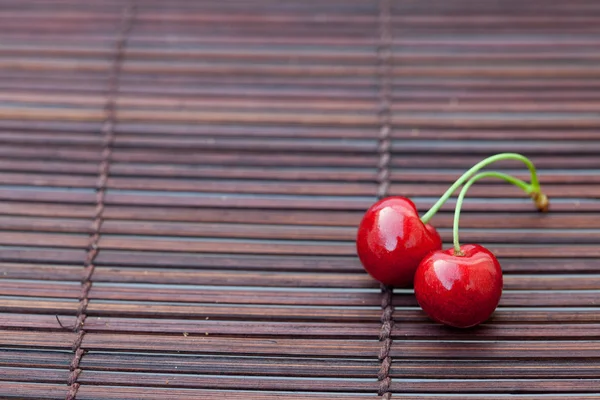 Two cherries on a bamboo mat — Stock Photo, Image
