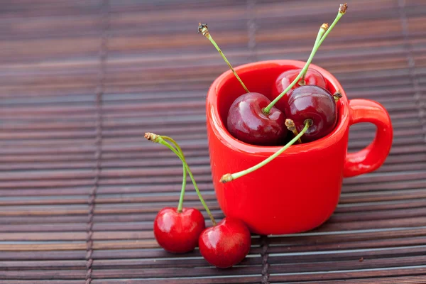 Kirsebær og rød kop på en bambusmåtte - Stock-foto