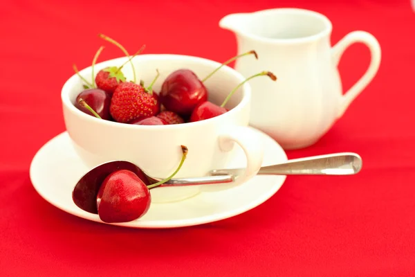 Süt kabı, kupa, fincan tabağı ve kaşık kırmızı bir arka plan üzerinde — Stok fotoğraf