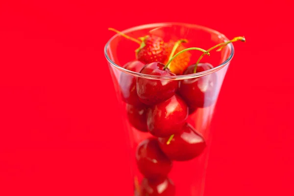 Vaso de cereza y fresa sobre fondo rojo — Foto de Stock