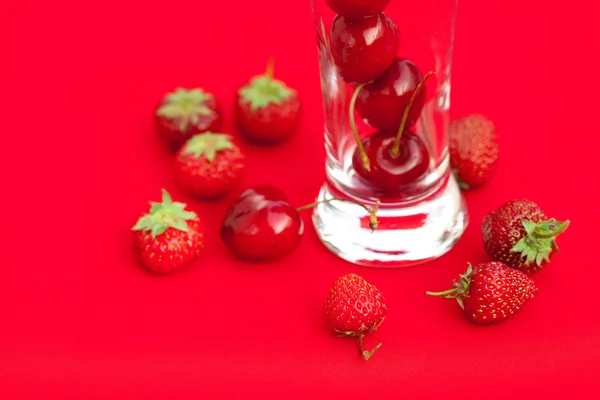 Glas van cherry en aardbei op een rode achtergrond — Stockfoto