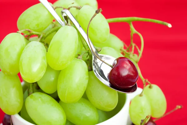Tasse mit Trauben und Kirschen auf rotem Hintergrund — Stockfoto