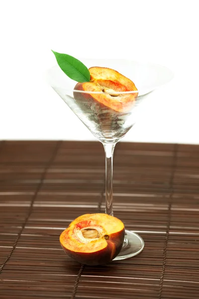Персик в бокале мартини на бамбуковом коврике — стоковое фото