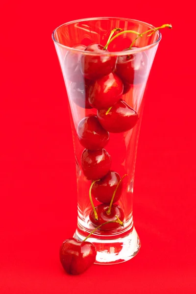 Glas mit einer Kirsche auf rotem Hintergrund — Stockfoto