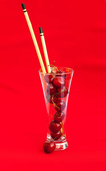 Vaso con cerezas y palillos sobre fondo rojo — Foto de Stock