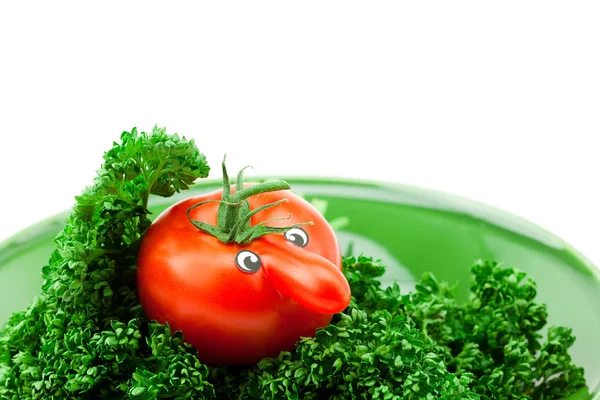 Tomato with eyes lying on a plate with greens — Stock Photo, Image