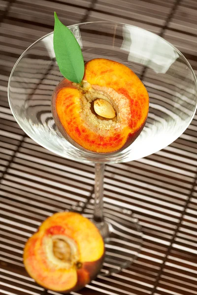 Персик с листом и бокалом мартини на бамбуковом коврике — стоковое фото