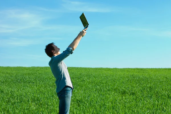 Man med laptop stående i ett fält — Stockfoto