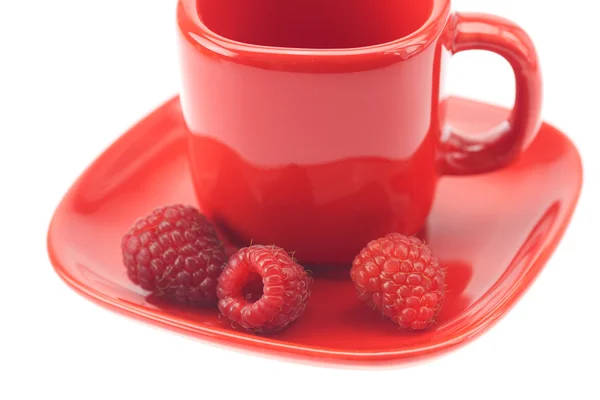 Framboesas em uma xícara vermelha e pires isolados em branco — Fotografia de Stock