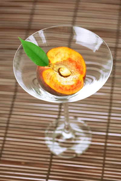 Персик с листом и бокалом мартини на бамбуковом коврике — стоковое фото