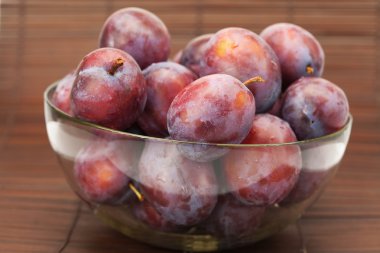 Plums in a glass bowl on a bamboo mat clipart