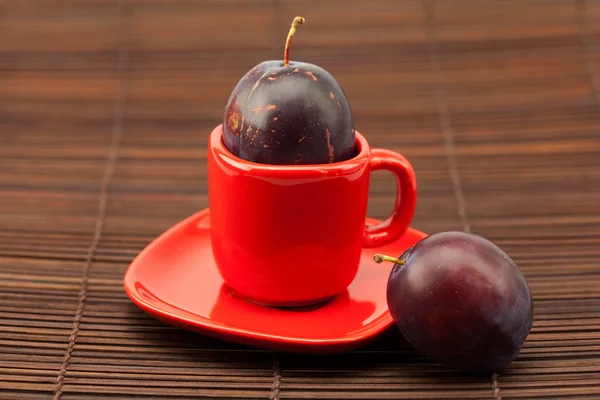 Plum in a cup and saucer on a bamboo mat — Stock Photo, Image