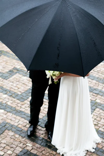 Panny młodej i pana młodego z bukietem kwiatów pod parasolem — Zdjęcie stockowe