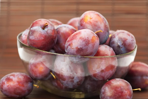 Plums in a glass bowl on a bamboo mat — Stock Photo, Image
