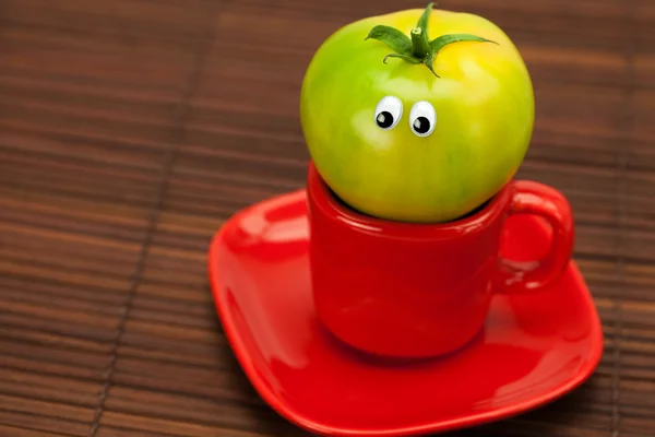 Tomato with eyes in the cup on a bamboo mat — Stock Photo, Image