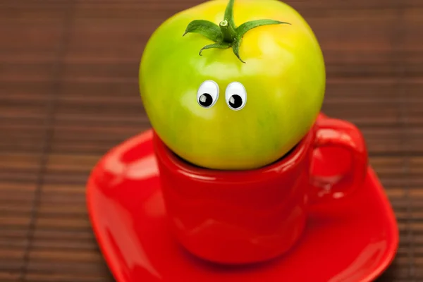 Tomato with eyes in the cup on a bamboo mat — Stock Photo, Image